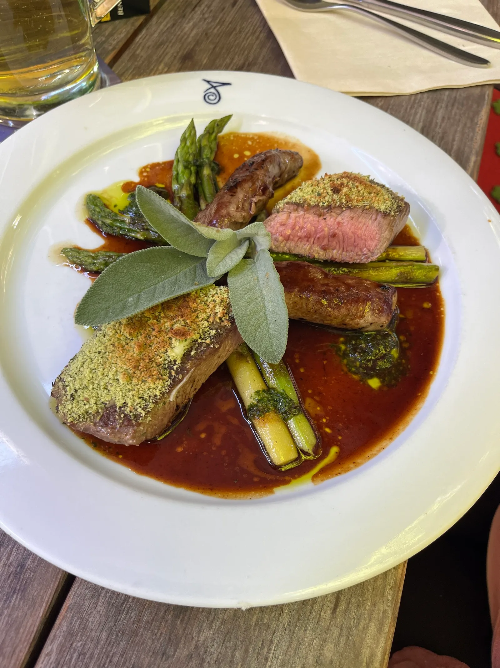 Lamm und Filet mit Kräuterkruste, grünem Spargel und Jus auf einem Teller mit dem Signet des Hauses