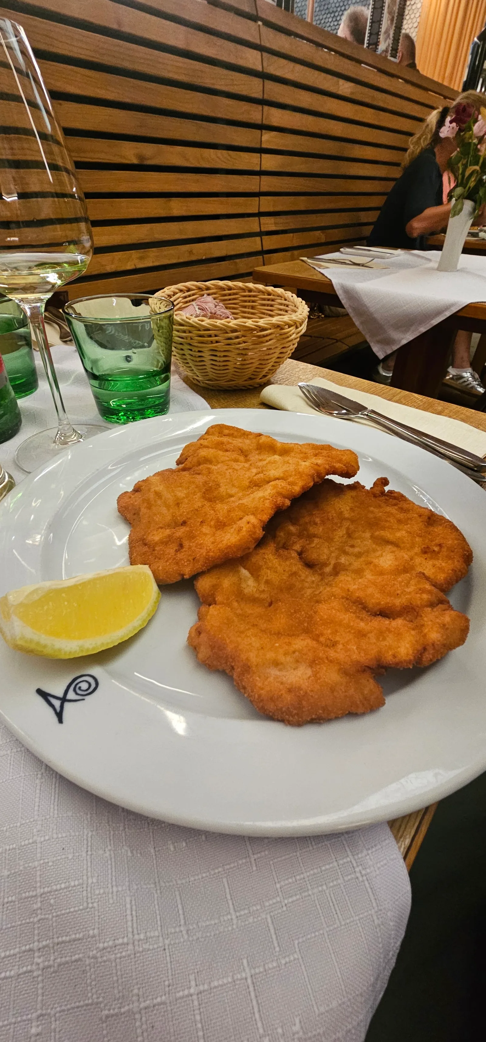 Zwei panierte Schnitzel mit Zitronenspalte auf einem Teller mit dem Signet des Hauses