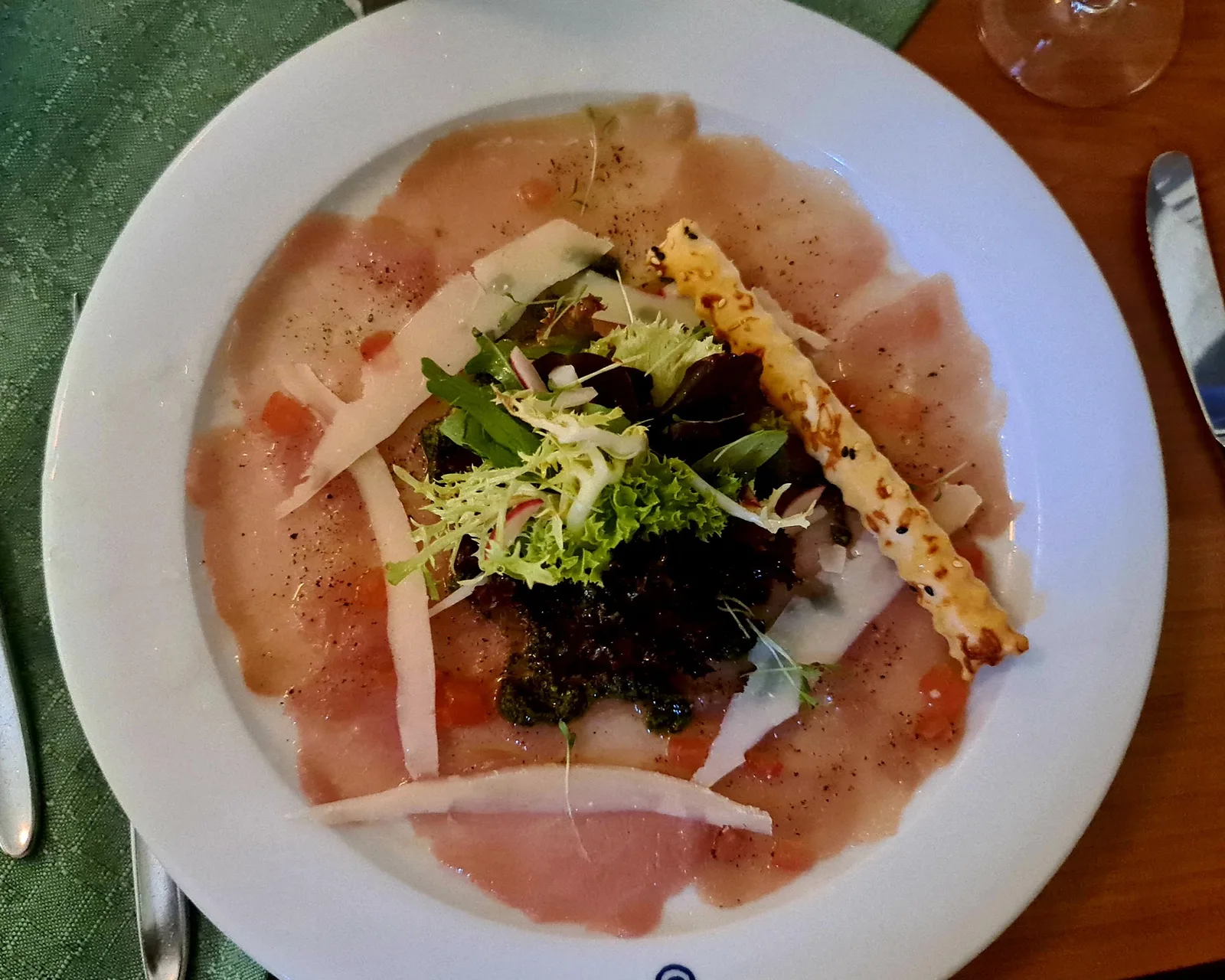 Carpaccio mit gehobeltem Hartkäse, Pesto und einem Salatbouquet in der Mitte
