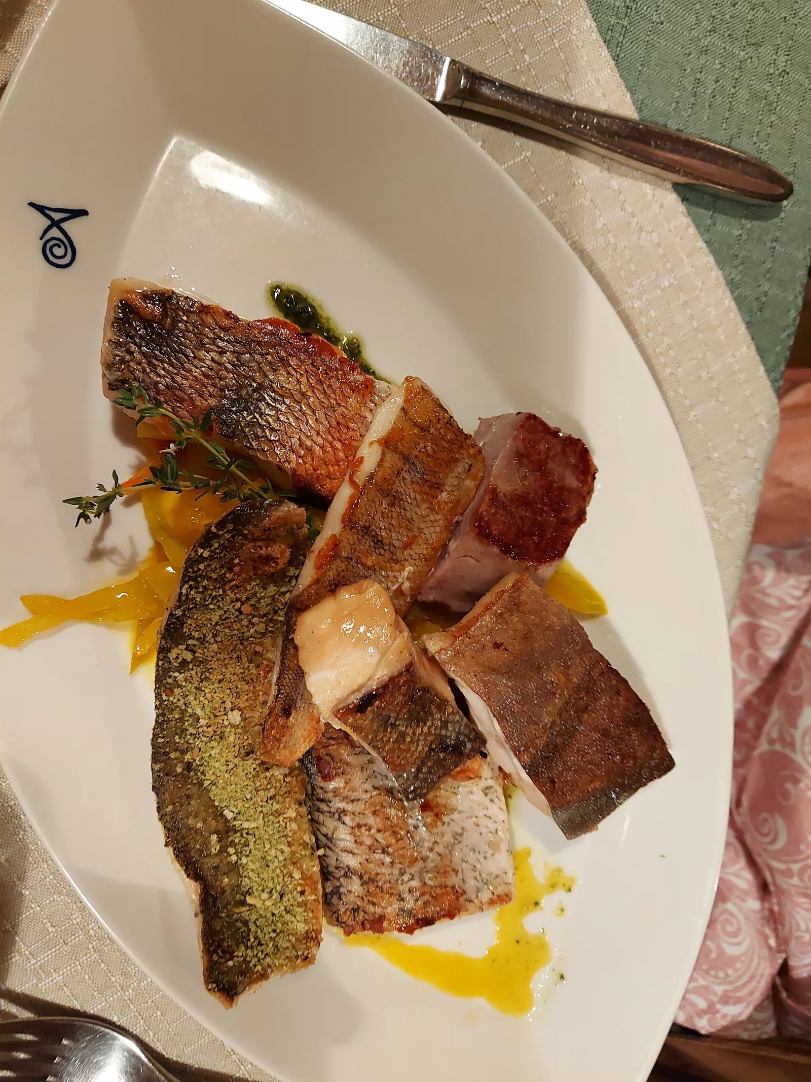 Variation von gebratenen Fischen auf einer länglichen Platte mit dem Signet des Hauses