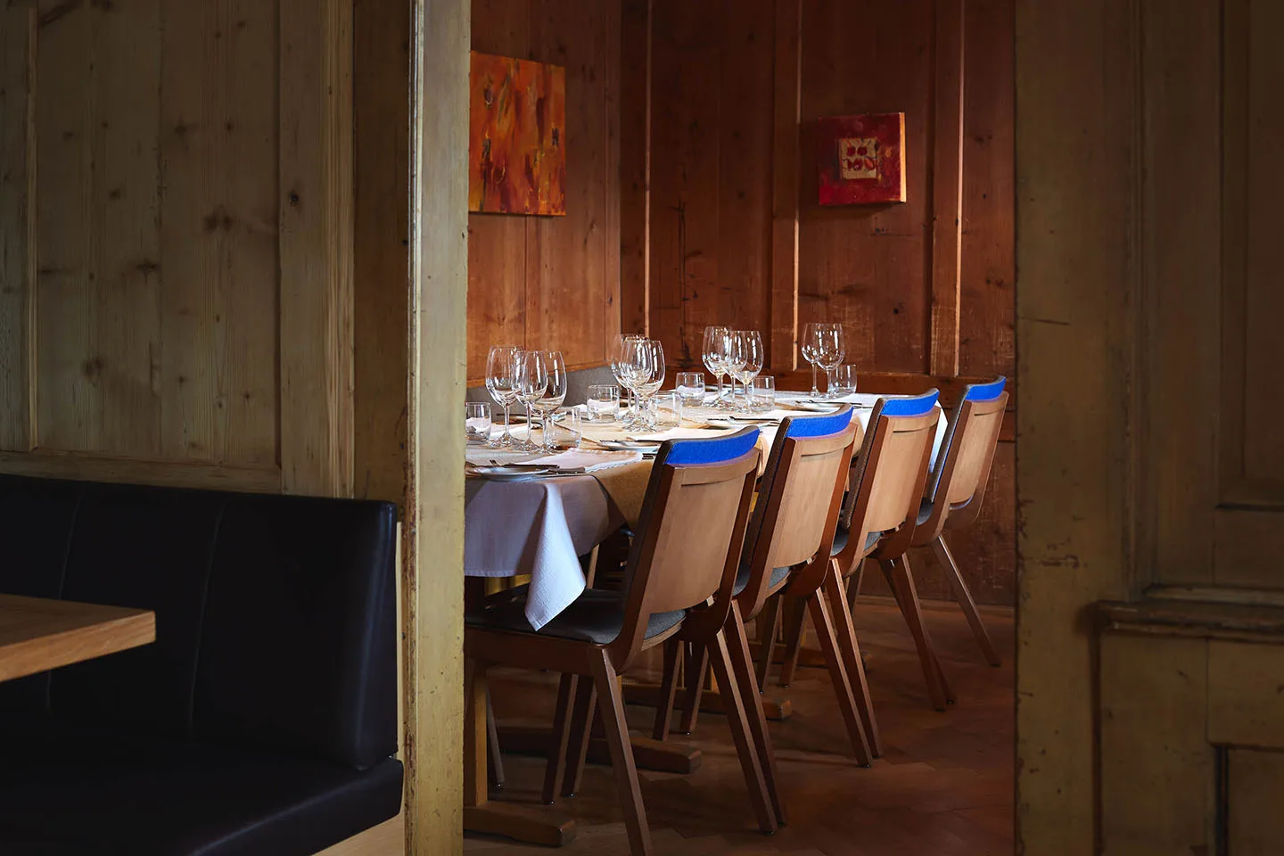Gedeckte Tafel vor altem Holztäfer, warmes Licht und blaue Stuhlkissen