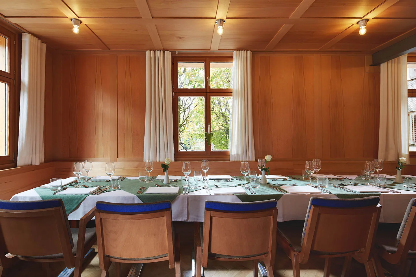 Heller Stubenraum mit Holztäfer, Fenster ins Grüne und einer Tafel mit grünen Läufern
