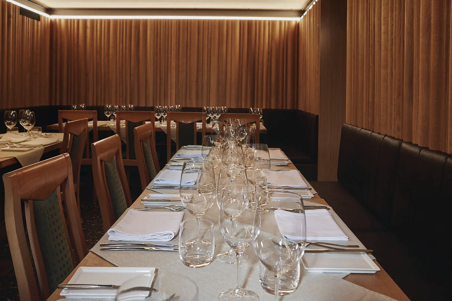 Heller Saal mit Holzlamellen an den Wänden und einer langen, gedeckten Tafel für große Runden